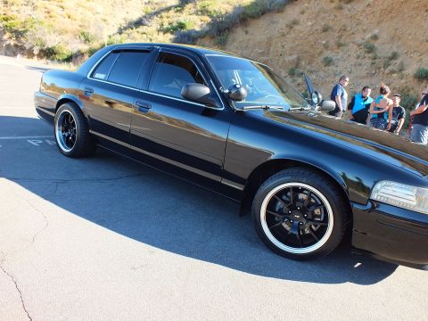2003 Ford Crown Victoria - Lowered black sedan shown in profile on pavement, people gathered in background at meet.