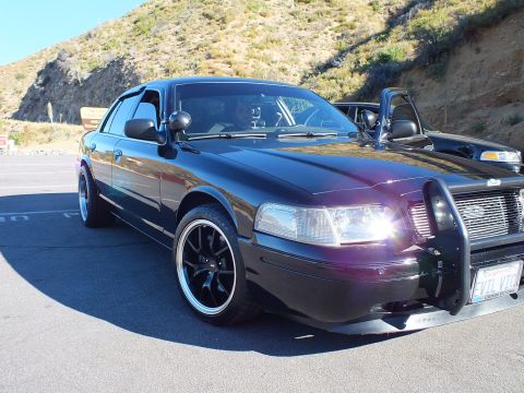 2003 Ford Crown Victoria - Maroon-tinted black sedan with push bar and lit headlights shows a front Nevada plate.