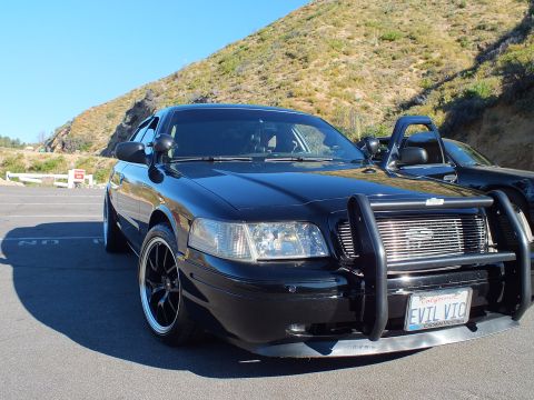 2003 Ford Crown Victoria - Black sedan with Ford grille badge and brush guard shows California EVIL VIC plate.