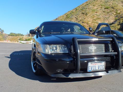 2003 Ford Crown Victoria - Head-on view of black sedan with brush guard, billet grille and California EVIL VIC plate.
