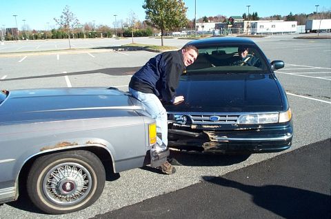 1991 Ford LTD Crown Victoria - A man leans on the hood of a damaged Ford Crown Victoria LTD while another person sits inside.