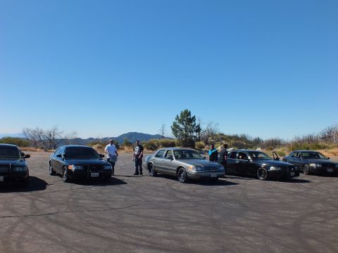 2003 Ford Crown Victoria - Black and silver full-size sedans line up on a dirt clearing as men talk beside them.