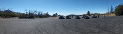 2003 Ford Crown Victoria - Distant cars and figures spread across a wide paved clearing in the hills.