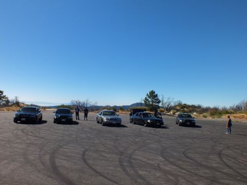 2003 Ford Crown Victoria - Several four-door sedans sit in a line on open pavement ringed by dry hills.