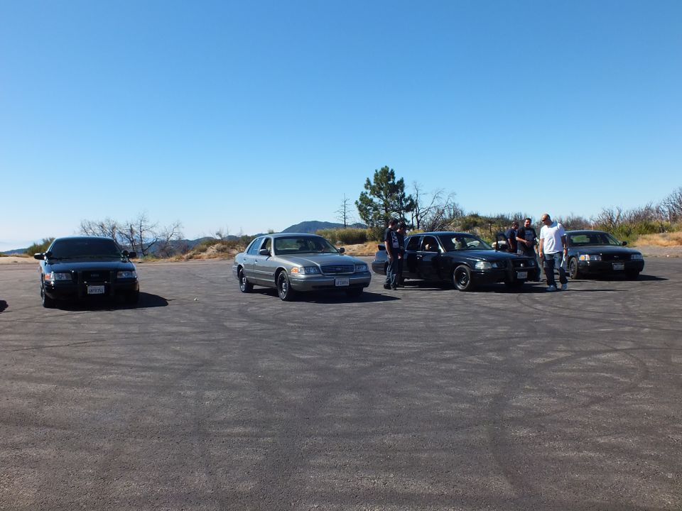 Black and silver full-size sedans parked on a hilltop with a group of men gathered