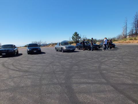2003 Ford Crown Victoria - Cars and a small crowd spread over an open paved clearing under blue sky.