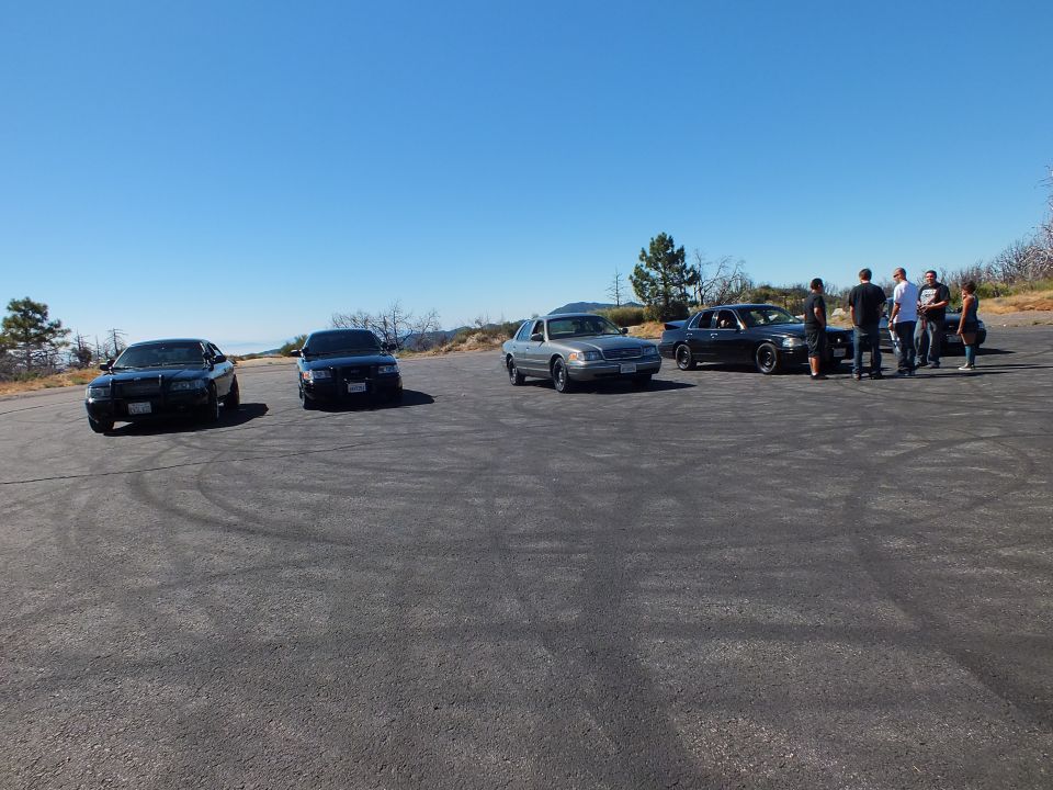Crown Victoria style sedans parked on a hilltop pad with a group of people talking
