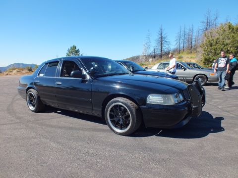 2003 Ford Crown Victoria - Side profile of lowered Panther sedan with grille guard, onlookers standing near rear, mountains behind