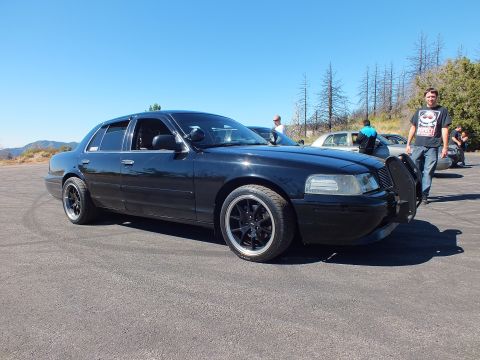 2003 Ford Crown Victoria - Lowered blacked-out sedan front-quarter on mountain lot, brush guard fitted, spectators in background