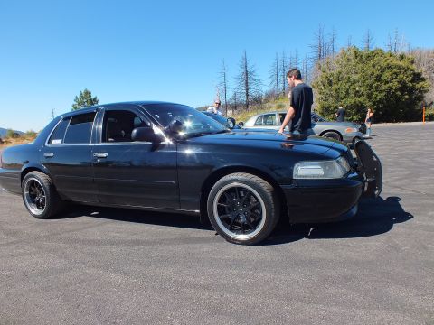2003 Ford Crown Victoria - Profile of lowered Panther sedan with grille guard, man resting on hood, clear blue sky