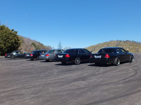 2003 Ford Crown Victoria - Lowered black and silver Panther sedans lined up from behind, dry hillside and clear sky