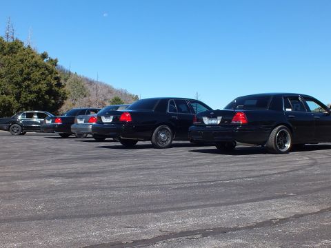 2003 Ford Crown Victoria - Lowered black Crown Victorias parked diagonally seen from behind, mountain lot, blue sky