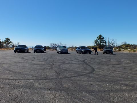 2003 Ford Crown Victoria - People stand near full-size cars on a tire-streaked overlook lot under deep blue sky