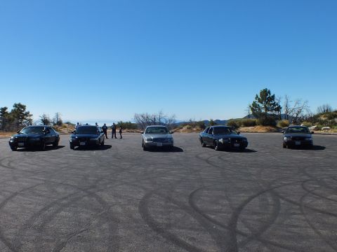 2003 Ford Crown Victoria - Crown Victoria and Grand Marquis cars staged on cracked asphalt below a ridge