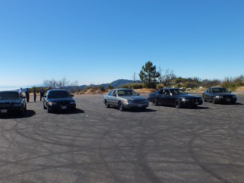2003 Ford Crown Victoria - Full-size cars and a small crowd on a tire-marked overlook under clear sky