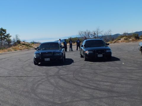 2003 Ford Crown Victoria - Pair of dark full-size cars on an overlook lot, hazy valley and ridgeline behind