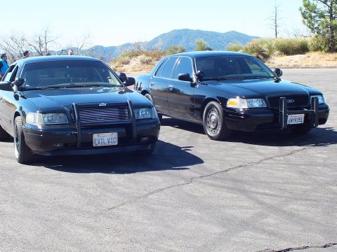 2003 Ford Crown Victoria - Two black full-size Ford and Mercury sedans parked nose-out before a mountain ridge