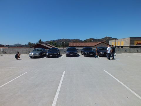 2003 Ford Crown Victoria - Front view of five sedans lined up on a rooftop parking deck under clear blue sky