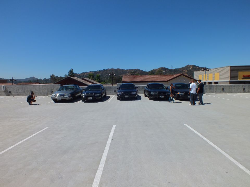 Five Ford and Mercury sedans parked across rooftop lot with hills and buildings behind