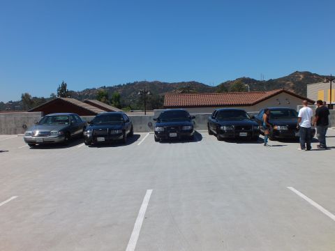 2003 Ford Crown Victoria - Black and silver full-size sedans parked on a rooftop deck as people stand nearby