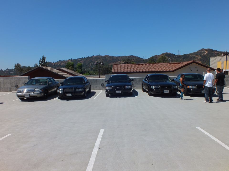 Row of black Ford Crown Victoria and silver Mercury sedans on rooftop lot with people