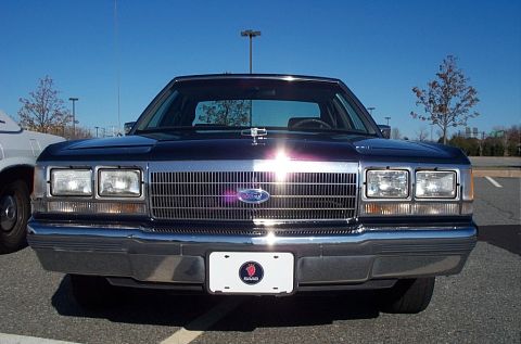 1991 Ford LTD Crown Victoria - Front view of a 1991 Ford Crown Victoria LTD, its distinctive chrome grille and dual rectangular headlights under a clear blue sky.