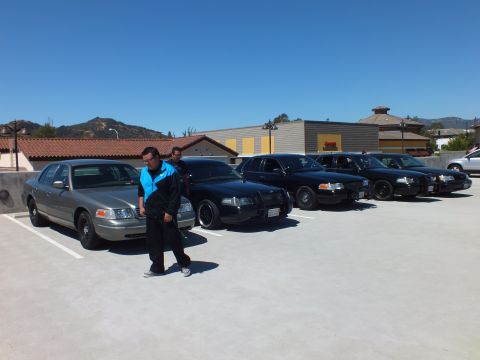 2003 Ford Crown Victoria - Person walks beside a lineup of silver and black full-size sedans on a paved deck