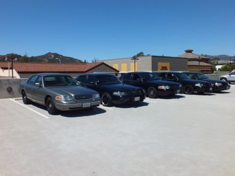 2003 Ford Crown Victoria - Angled row of silver and black full-size Ford and Mercury sedans on a parking deck