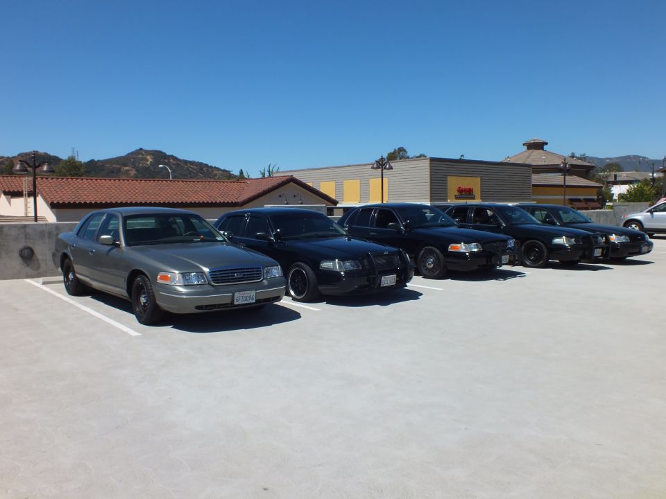 Silver Mercury Grand Marquis leading row of black Ford Crown Victoria sedans on rooftop lot