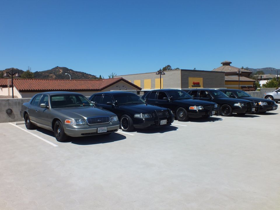 Silver Ford Crown Victoria and four black sedans angled across rooftop parking deck