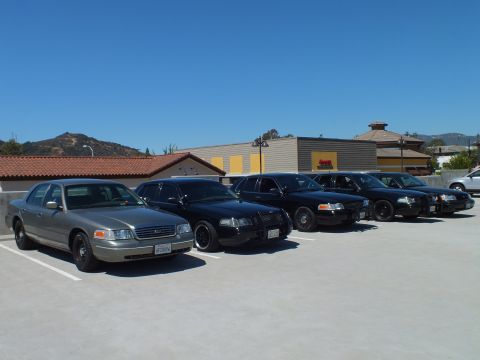2003 Ford Crown Victoria - Lineup of silver and black Ford Crown Victoria sedans angled on a paved rooftop deck
