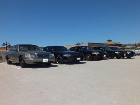 2003 Ford Crown Victoria - Silver Crown Victoria on black wheels ahead of black sedans on a sunny parking deck