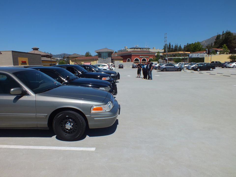 Silver Ford Crown Victoria with black wheels parked at angle on rooftop lot with stores behind