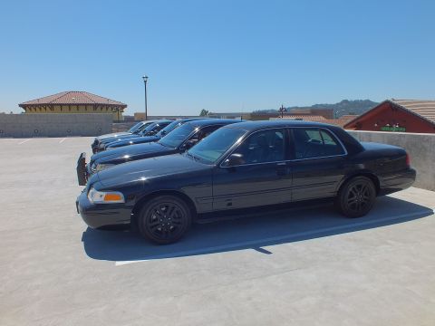 2003 Ford Crown Victoria - Profile of a blacked-out Ford Crown Victoria on a rooftop parking level under clear blue sky.