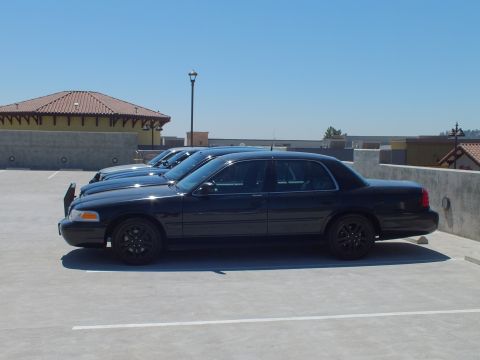2003 Ford Crown Victoria - Side view of multiple black Crown Victorias staged on a concrete parking level.