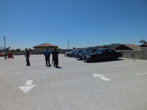2003 Ford Crown Victoria - Wide shot of a rooftop lot with three men and a row of dark sedans against hills.