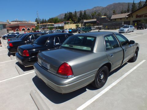 2003 Ford Crown Victoria - Rear three-quarter of a gray Crown Victoria with steel wheels parked among black sedans.