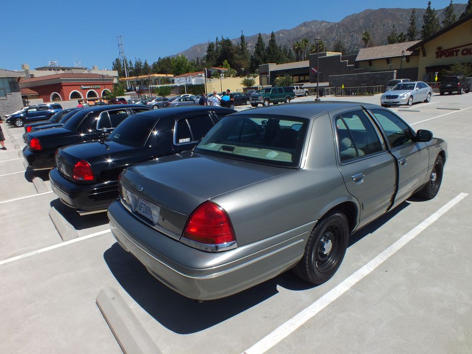 Gray Ford Crown Victoria sedan rear quarter beside black sedans in parking lot