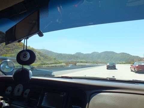 2003 Ford Crown Victoria - Driver POV on a freeway through mountains, eight-ball charm on the mirror, gauge pod on dash.
