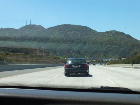 2003 Ford Crown Victoria - Following a black sedan on an open freeway with hillsides on both sides.