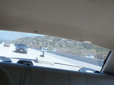 2003 Ford Crown Victoria - View out a sedan rear window of a freeway and brush-covered hills, phone holder on the deck.