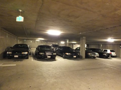 2003 Ford Crown Victoria - Row of dark Crown Victoria sedans under a lit exit sign in a subterranean garage.