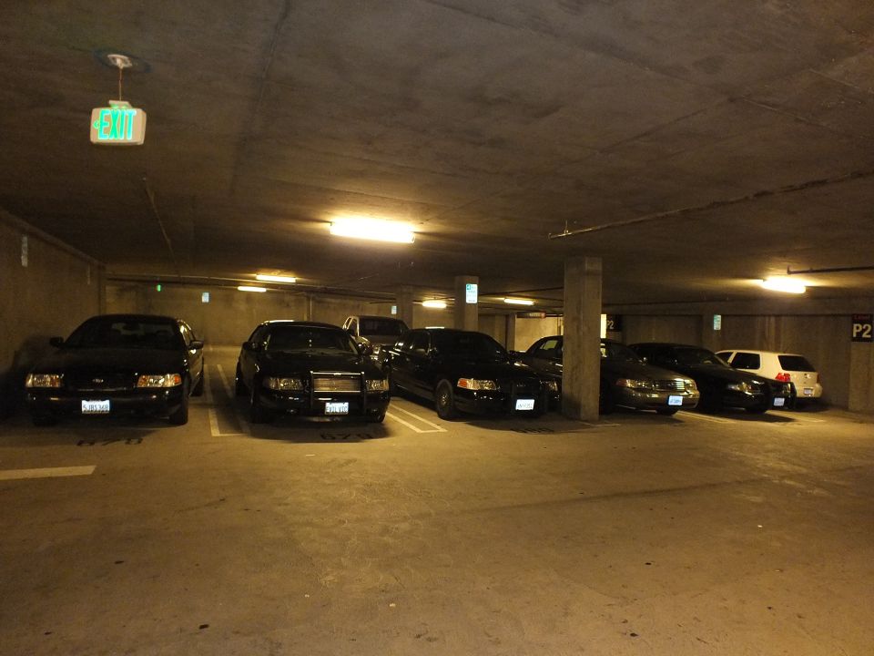 Black sedans parked in a dim underground parking garage with exit and P2 signs