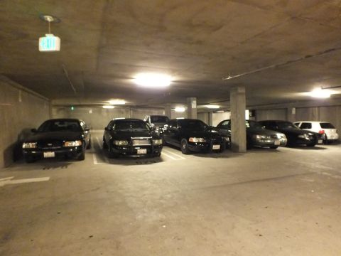 2003 Ford Crown Victoria - Front views of dark sedans parked beneath a lit exit sign in a basement garage.