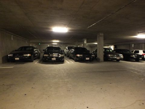 2003 Ford Crown Victoria - Five dark sedans lined up facing forward on a concrete garage level.