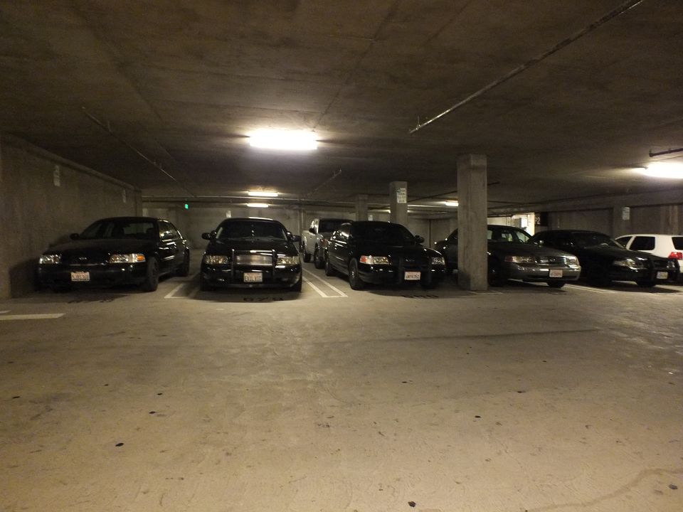 Black Ford Crown Victoria sedans parked head-in across a dim parking garage