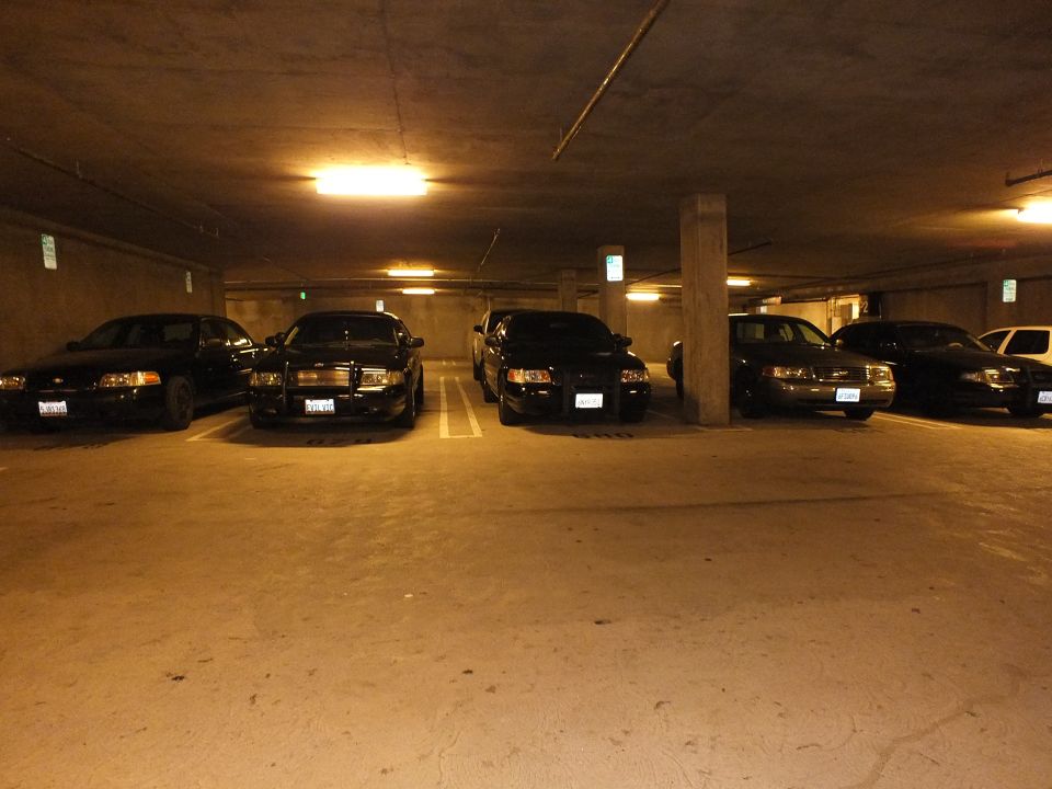 Black Ford Crown Victoria sedans parked under warm garage lighting