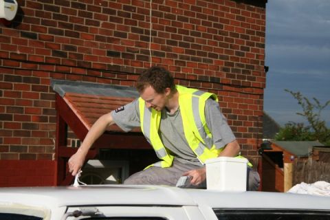 1989 Ford Bronco - A man is seen working on the roof of a white vehicle, with a brick building in the background.