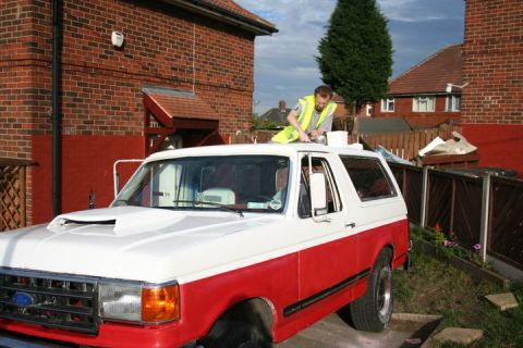 1989 Ford Bronco - A man works on the roof of a two-tone red and white Ford Bronco parked in a driveway.