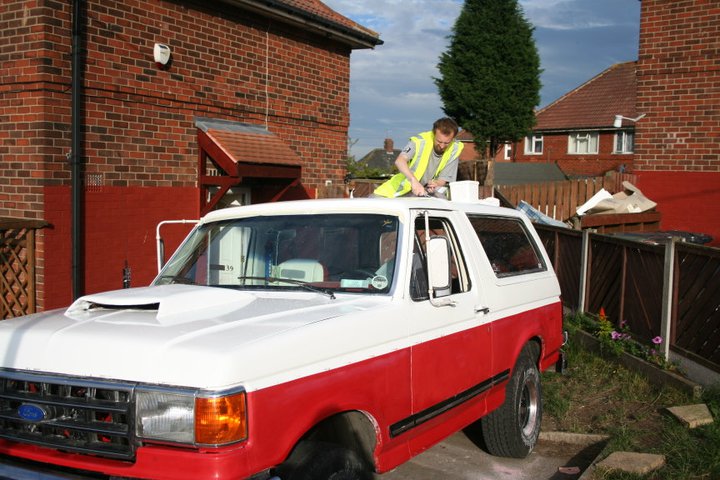 Two-tone red and white Ford Bronco with a man on the roof